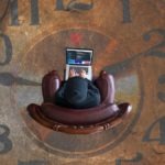 man wasting time on laptop sitting in middle of painted clock