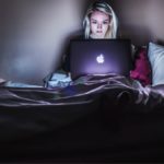 woman sitting on bed using laptop in dark