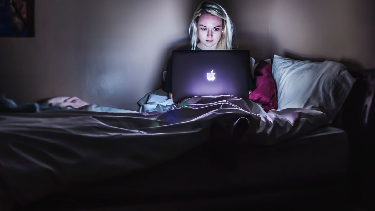 woman sitting on bed using laptop in dark