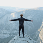 man-with-arms-wide-open-standing-on-top-of-cliff