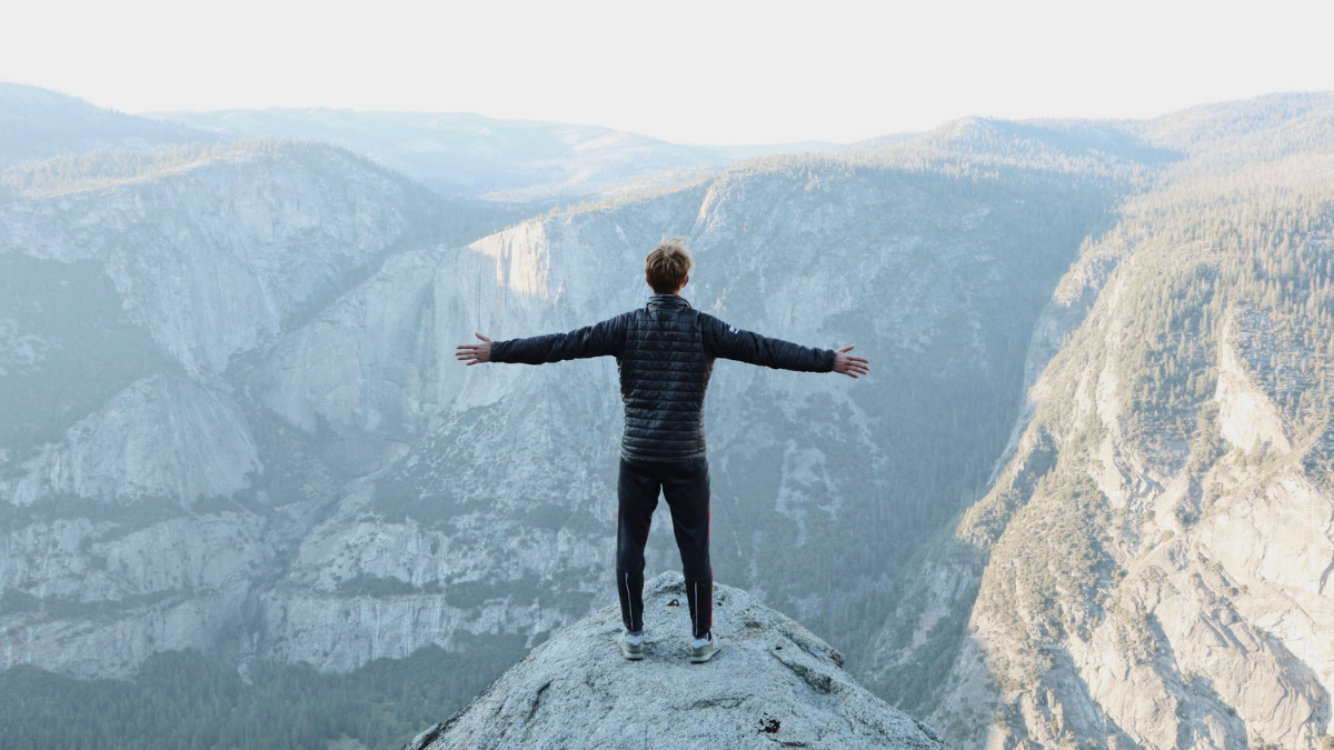 man-with-arms-wide-open-standing-on-top-of-cliff